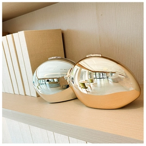 Polished gold and silver oval metal clutch bags with mirror finish on a wooden shelf