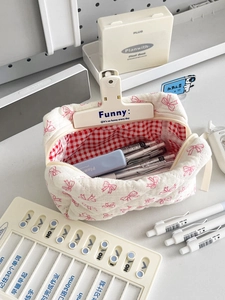 Close-up of quilted cotton bow makeup bag with red checkered lining and stationery items