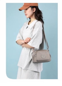 Detail view of light grey nylon crossbody bag with multi-zipper compartments on a casual model