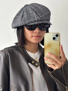 Mirror selfie showing a black and white checkered newsboy cap with vintage leather jacket