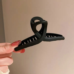 Close-up of a matte black shark hair claw clip held by a hand with red nails