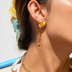 Detail of gold heart stud earrings with tassel chains and zircon accents on a model
