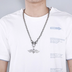 Macro view of winged skull pendant and woven steel chain on model's chest
