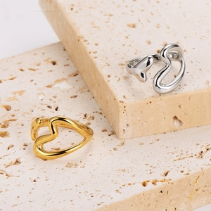 Gold and silver hollow heart open rings displayed on a minimalist beige stone pedestal