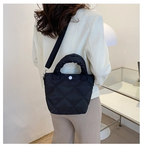 Detail of black quilted handbag with pleated handle and adjustable nylon shoulder strap