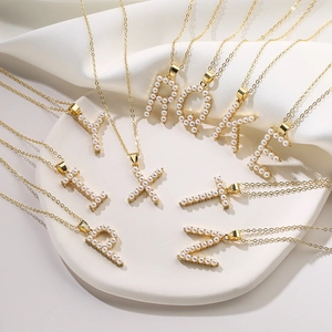 Elegante collana d'oro con pendente con iniziale in perle su sfondo di seta bianca