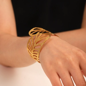 Dettaglio del bracciale rigido largo dorato 18K con trama a foglia traforata sul polso