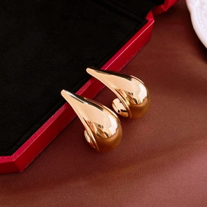 Detailed close-up of gold water drop earrings with polished finish on satin fabric