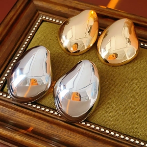 Close-up of polished gold and silver waterdrop earrings on a green velvet tray