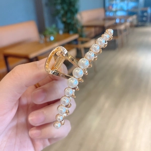 Close-up of golden metal hair claw clip with elegant white pearls held in natural light