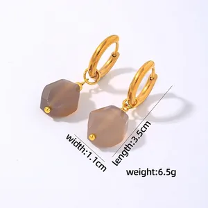 Macro detail of geometric drop earrings with gold hoops and grey hexagonal stone pendants