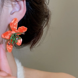Detailed close-up of large orange floral stud earrings with handmade beaded details