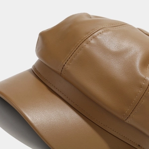 Close-up of brown PU leather newsboy cap showing fine stitching and glossy texture