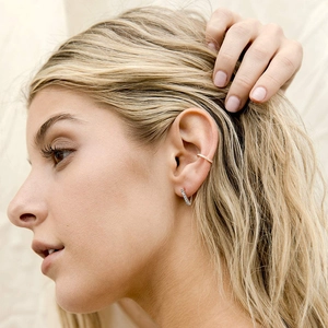 Elegant gold diamond ear cuff and silver round stud earrings worn by model on fabric background