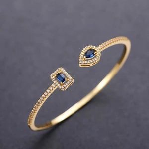 Detail of gold open cuff bracelet with pear-cut and rectangular blue zircon stones