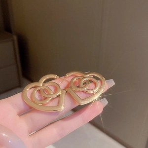 Detail of gold heart earrings featuring an interlocking C pattern with luxury hollow design