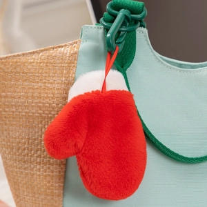 Close-up of a red and white plush glove ornament hanging on a woven bag with a green hook