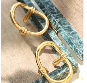 Detailed close-up of golden oval knot earrings on a textured blue jewelry box