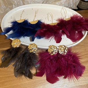 Detail view of colorful feather tassel earrings in blue, red and grey with gold metal accents