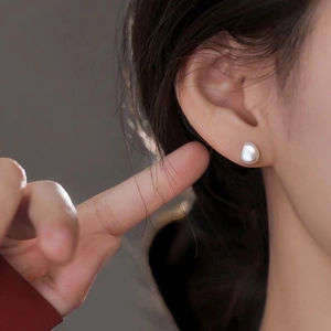 Detailed close-up of a white Baroque pearl earring worn on the ear with soft lighting