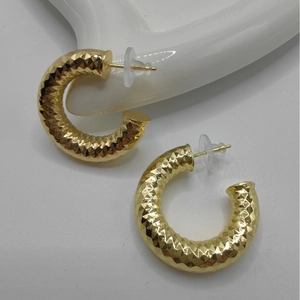 Polished chunky gold C-shaped hoop earrings with faceted geometric texture on white ceramic