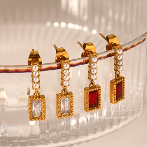 Elegant gold-plated drop earrings with white pearls and red zircon on a glass rim