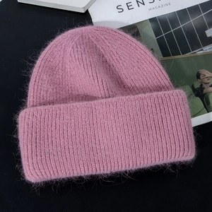 Detail of pink knitted rabbit fur winter hat with soft plush texture on black surface