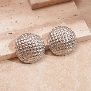 Close-up of silver dome stud earrings featuring a textured diamond quilted pattern on stone