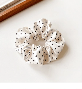 Detail of cream polka dot satin scrunchie with soft pleated texture and glossy finish