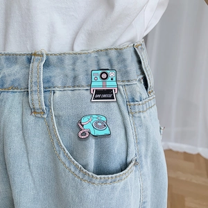 Retro Polaroid camera and vintage rotary phone enamel pins set on denim pocket edge
