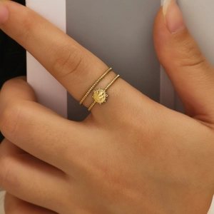 Close-up of golden double-layer stainless steel ring with sun coin charm on finger