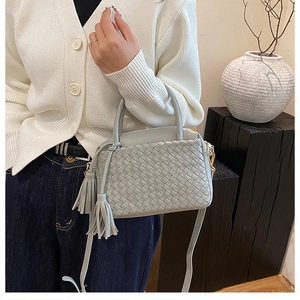 Detail of grey woven leather bag with dual tassels and intricate knit texture