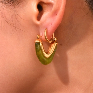 Macro shot of 18K gold V-shaped earrings with dark green resin inlay on the ear