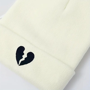 Close-up of white knitted beanie featuring a black broken heart embroidery detail