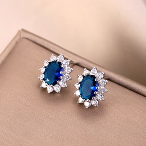 Macro shot of oval blue gemstone stud earrings with white zircon halo on metallic box