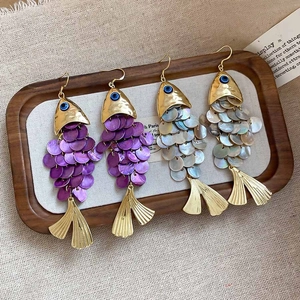 Detailed macro view of fish-shaped shell drop earrings with colorful sequins and gold plating