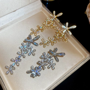 Macro shot of silver and gold flower tassel earrings with zircons on a beige jewelry box