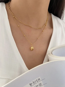 Close-up of double-layer gold teardrop pendant necklace worn on a white V-neck top
