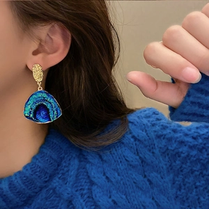 Macro shot of stylish fan-shaped earrings with blue-green gradient on a model