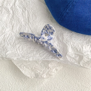 Detail of blue and white porcelain pattern hair claw clip on textured white paper
