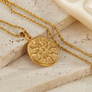 Macro shot of a golden sun totem pendant on a twist chain against a silk fabric background