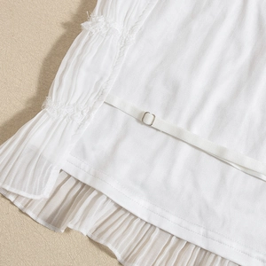 Detail shot of white knitted top featuring delicate ruffles and metal buckle strap adjustment