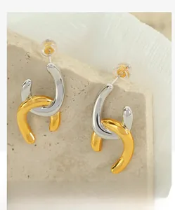 Detail of minimalist gold and silver intertwined geometric U-shaped metal earrings