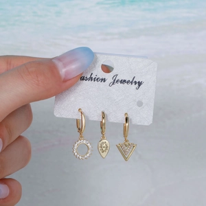 Minimalist gold hoop earring set with zircon star moon pendants held at a beach