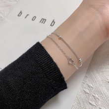 Close-up of double-layer silver bracelet with heart pendant and beads on woman's wrist