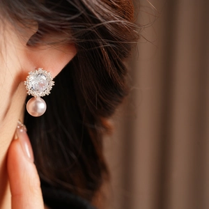 Close-up of pearl drop earring with zircon flower cluster on female model