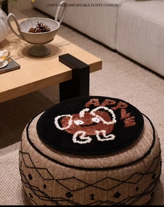 Soft round black plush seat cushion with brown cartoon apple character in home interior