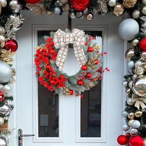 Christmas wreath with red berries and bow hanging on a white wooden front door