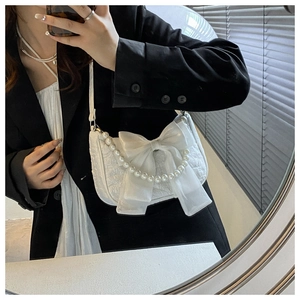 Detail of white bow pearl handbag worn with black blazer for high contrast style