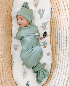 Detail of soft cotton baby swaddle set with knotted hat in sage green in a woven basket